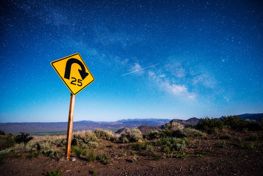 A road sign is illuminated at night with a shooting star and the Milky Way overhead on Monitor Pass in the Sierra Nevada mountains near Markleeville, California.