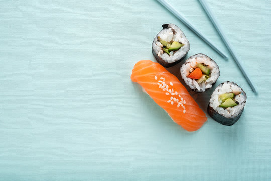 Sushi set with salmon nigiri and roll with cucumber and vegetables with chopsticks on a blue background, for the sushi bar menu