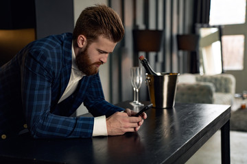 Profile of handsome stylish man in blue suit in cage at home. Sitting in modern black kitchen with smart phone in hand.