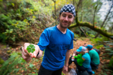 A man stands on a trail smiling holding a four-leaf clover while backpacking the Lost Coast Trail in Sinkyone Wilderness State Park in Northern California.