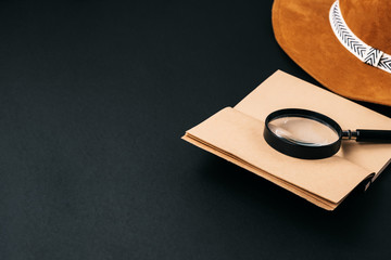 Notebook with craft paper and a magnifying glass on a black background with copy space