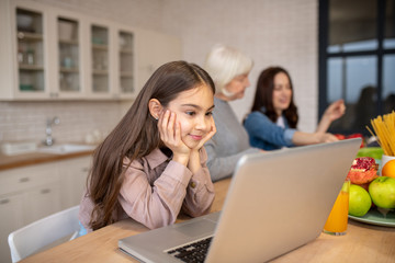 Daughter looking at a laptop at a table in the kitchen.