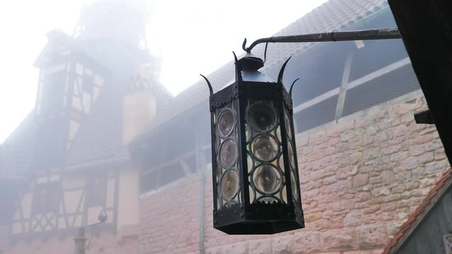 Farol de hierro mecido por viento g&eacute;lido en castillo terror cubierto de niebla