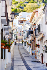 Fototapeta na wymiar Hillside village of Mijas, empty street leading up, white washed residential houses with hanging plants on walls, Málaga, Costa del Sol, Spain