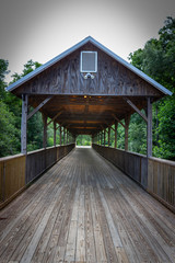 A wooden, covered bridge with green trees in the background.