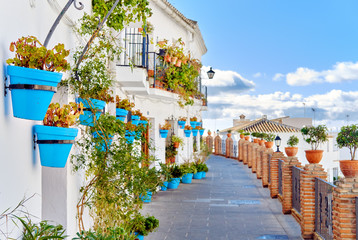 Idyllic scenery empty picturesque street of small white-washed village of Mijas. Path way decorated with hanging plants in bright blue flowerpots, Costa del Sol, Andalusia, Province of Málaga, Spain. - obrazy, fototapety, plakaty