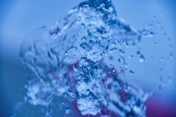 Photography of water white colored. Fresh jets of water fly up. Spray is flying in all directions from small fountains. Focus on stream of water.  Background is dark and blurry.