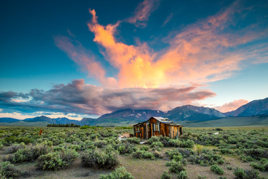 A magnificent sunset explodes over an old abandoned cabin in the desert with the Sierra Nevada mountains in the background near Lee Vining, California.