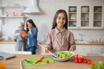 Little girl in the kitchen showing cooked salad.
