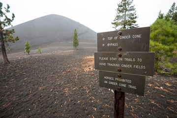 A trail sign points the way to Cinder Cone volcano (pictured in the background) on a stormy day in Lassen Volcanic National Park, California.