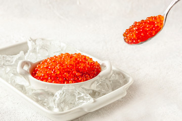 Trout caviar in a white bowl with ice on a white background.