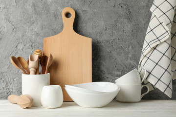 Tableware, cutlery and wooden board on white table against gray background, space for text