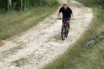 Naklejka premium A casually dressed man rides a mountain bike on a rural road.
