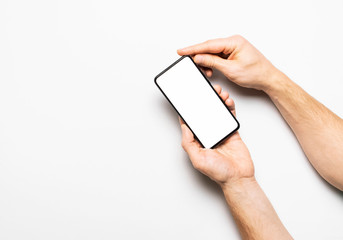 Male hands hold a modern black smartphone with white blank screen on light gray background. Modern technology, phone, gadget in hands, touch screen, template for your design. Mockup