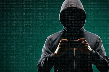 Anonymous computer hacker with a smartphone over abstract digital background. Obscured dark face in mask and hood. Data thief, internet attack, darknet fraud, dangerous viruses and cyber security.