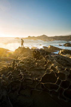A sunset view of a man standing around tafoni honeycomb rocks in Salt Point State Park, along the Sonoma Coast in California.