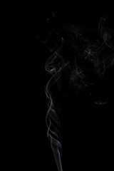 Delicate column of smoke from incense stick isolated on black background, selective focus