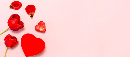 Red tulips, red heart shaped gift box, confetti on pastel pink background top view Flat lay copy space. Mother's Day, Valentines Day, birthday, holiday background. Spring flowers, Lovely greeting card