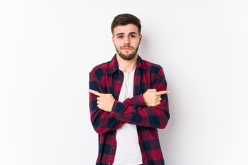 Young caucasian man posing in a white background isolated points sideways, is trying to choose between two options.