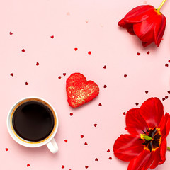 Red tulips, red heart shaped gift box, cup of coffee, macaron cake, confetti on pastel pink background top view Flat lay. Mother's Day Valentines Day birthday holiday background. Lovely greeting card