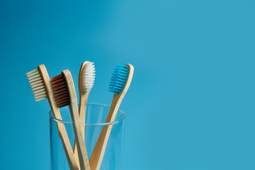 Wooden toothbrushes with a glass cup on a blue background with copy space. Environmental awareness, pollution and zero waste concept. Closeup.