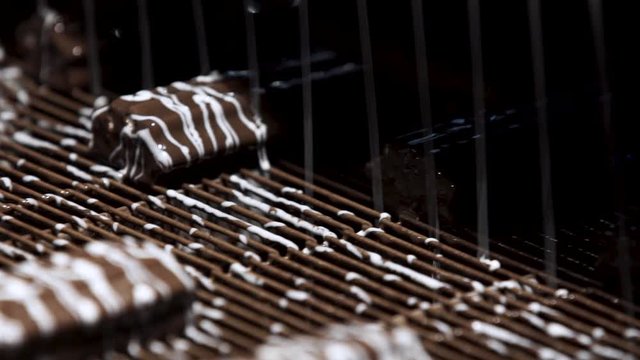 Machine pouring liquid on candies. Conveyor belt with brown sweets. Production of high-quality dessert. Under a flow of chocolate.