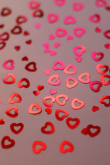 Red heart shaped confetti on pale pink background. Love and valentine concept. Selective focus. 