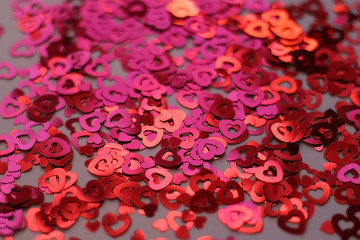 Red heart shaped confetti on pale pink background. Love and valentine concept. Selective focus. 