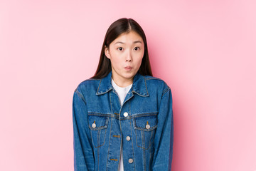 Young chinese woman posing in a pink background isolated shrugs shoulders and open eyes confused.