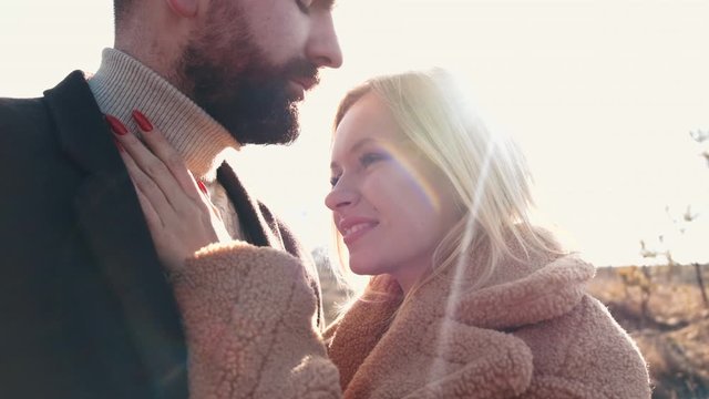 European couple is hugging at sunset face to face. The woman is caressing the man's beard by hand.The sunbeams are lighting them up.