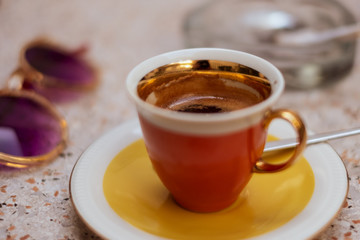 An orange espresso cup on a table in an outdoor cafe. Warm, bright and summery atmospehre.