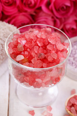 Glass bowl with red sea salt. Pink roses in the background.