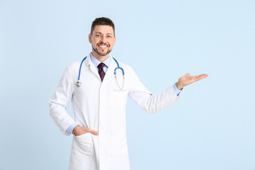 Portrait of male doctor showing something on color background