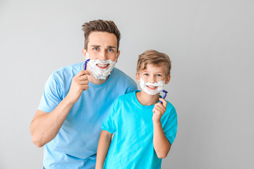 Father and his little son shaving against grey background