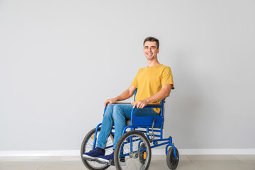 Handicapped young man in wheelchair near light wall