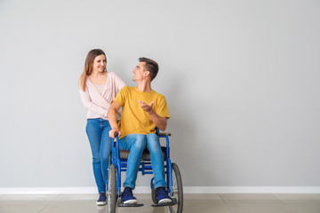 Handicapped young man in wheelchair and his wife near light wall