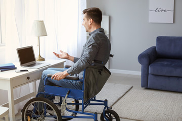 Handicapped young man in wheelchair using laptop at home