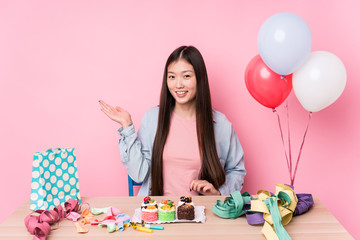 Young chinese woman organizing a birthday isolated showing a copy space on a palm and holding another hand on waist.