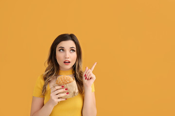 Portrait of thoughtful young woman with burger on color background