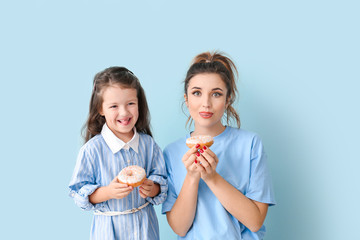 Beautiful young woman and little girl with donuts on color background