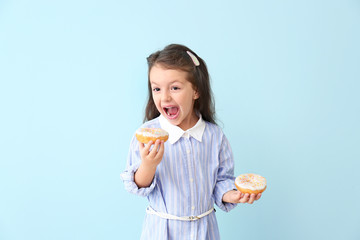 Funny little girl with donuts on color background