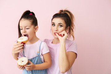 Beautiful young woman and little girl with donuts on color background