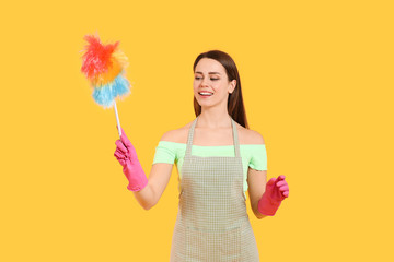 Young housewife with dust brush on color background