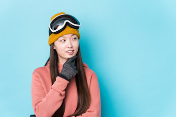 Young chinese woman wearing ski clothes isolated relaxed thinking about something looking at a copy space.