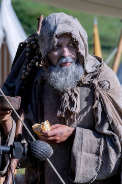 Middle-aged, bearded and ragged beggar, wandering a camp, looking for food