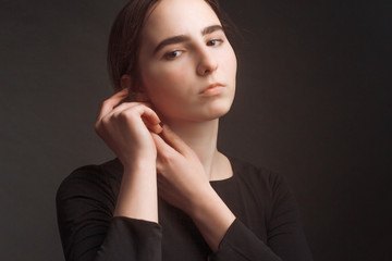 The brown-haired girl in dark clothes, a portrait on a dark gray Studio background. Warm toning.