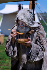 Middle-aged, bearded and ragged beggar, wandering a camp, looking for food