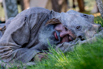 Middle-aged, bearded and ragged beggar, wandering a camp, looking for food