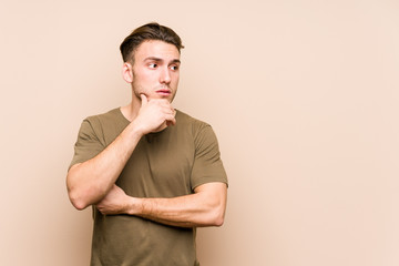 Young caucasian man posing isolated thoughtful looking to a copy space covering mouth with hand.