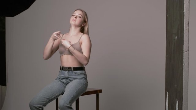 backstage of sexy caucasian woman posing in beige lingerie and blue jeans on white studio background. model tests of pretty girl in bra. attractive female sitting on chair fixing her long hair